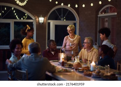 Happy Multi-ethnic Extended Family Talking While Gathering For Dinner At Dining Table On A Patio. 