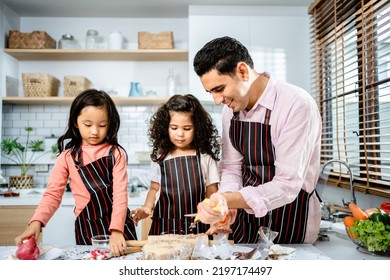 Happy Multiethnic Family Cooking Creams Cake Together In The Kitchen At Home. A Father Teaches Daughters To Make Homemade Desserts, Enjoy Leisure Activities Time