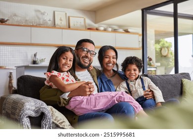 Happy multiethnic family having fun at home, parents and little children sit on sofa together and looking at camera. Portrait of indian family sitting on couch while laughing together. - Powered by Shutterstock