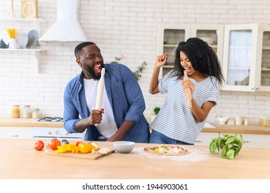 Happy Multiethnic Family In The Kitchen Having Fun And Cooking Together, Healthy Food At Home, Young Joyful Couple Have Fun Dancing And Singing With Rolling Pin While Set The Table For Breakfast