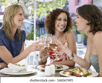 Happy multiethnic female friends toasting wine at outdoor cafe