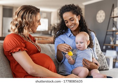 Happy multiethnic friends with child sitting on couch. Pregnant mother relaxing with her girlfriend. Pregnant lesbian gay couple with one toddler son, assisted fertilization and adoption concept.  - Powered by Shutterstock