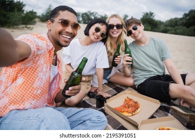 Happy Multiethnic Friends In Sunglasses Holding Beer Near Tasty Pizza On Beach