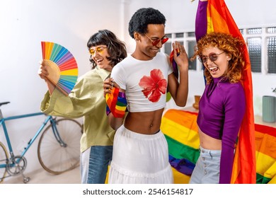 Happy multi-ethnic and gender diverse friends celebrating pride party at home wearing sunglasses and using hand fan and rainbow flags while dancing - Powered by Shutterstock