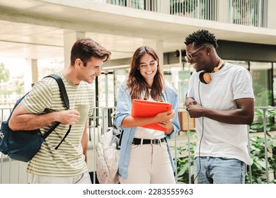 Happy multiethnic group of teenage students talking about the homeworks after the class at university campus. Three young people smiling, having a friendly conversation together standing at the school - Powered by Shutterstock