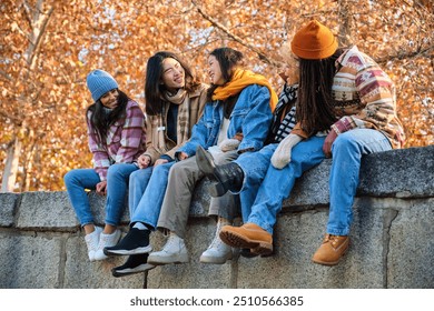 Happy multi-ethnic group of young hipster diverse student friends having fun while hanging out sitting together outdoors. Friendship concept. - Powered by Shutterstock