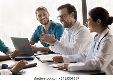 Happy multiethnic medical colleagues talking and laughing at meeting table, discussing successful doctor job, medical practice, work cases, having fun, enjoying networking - Powered by Shutterstock