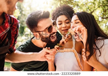 Happy multiethnic millennials playing together eating skewers and eating together skewers in the countryside at picnic - focus on African American woman - people, food and drink lifestyle concept