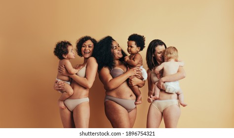 Happy multi-ethnic mothers with postpartum bodies holding their babies. Three women with their children standing together.