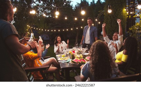 Happy multi-ethnic people having fun at garden at night. Caucasian boys and girls drinking and eating while talking outdoor. African American female laughing. Asian girl with watermelon. Party concept - Powered by Shutterstock