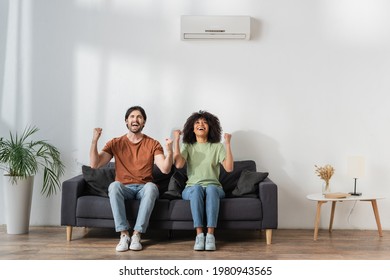 happy multiethnic rejoicing while sitting on couch in modern living room, hvac concept