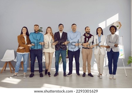 Happy multiethnic team holding hands united by goal looking at camera standing in row, smiling diverse millennial business people group tied connected together as unity trust support teamwork concept