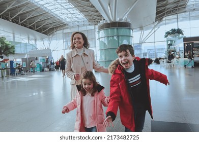 Happy Multiethnic Woman With Her Children Running In Airport Arrivals Terminal Waiting Room. Long-awaited Family Reuniting Concept