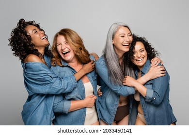 Happy multiethnic women in underwear and denim shirts embracing isolated on grey, body positive concept