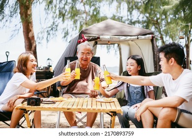 Happy Multi-generation Asian Family Enjoys Cheers Orange Juice Together During Picnic And Camping On Tropical Beach. Summer Activity. Relax And Outdoor Activity Lifestyle Family Concept