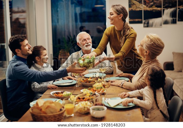 Happy\
multi-generation family enjoying in a lunch together at home. Focus\
is on young woman serving salad at dining table.\
