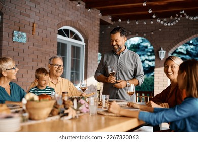 Happy multigeneration family enjoying in meal at dining table on terrace. Focus is on father holding a toast. - Powered by Shutterstock