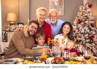 Happy multi-generation family enjoying spending winter holiday season together, having fun holding balloons shaped as numbers 2025 while having Christmas dinner at home - Powered by Shutterstock