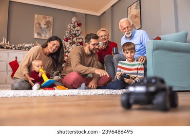 Happy multi-generation family having fun spending Christmas day together at home, father teaching son how to play with remote controlled toy car - Powered by Shutterstock