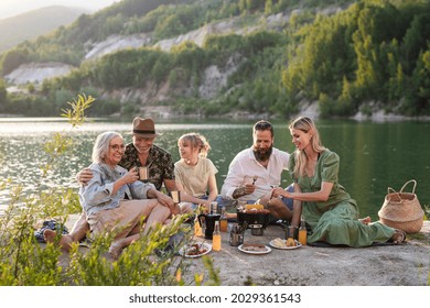 Happy Multigeneration Family On Summer Holiday Trip, Barbecue By Lake.