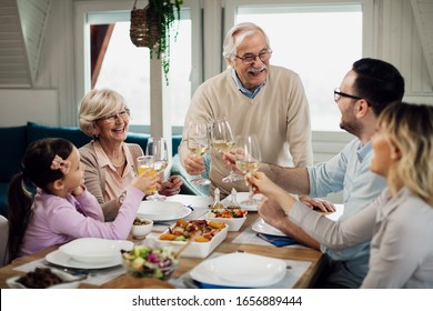 Happy Multi-generation Family Toasting During Lunch Time At Dining Table. Focus Is On Senior Couple. 