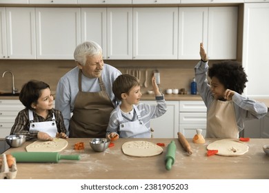 Happy multigenerational family cooking in kitchen. Three cute multiethnic boys prepare homemade cookies with help of older great-grandpa, have fun, enjoy process, dessert preparation, giving high five - Powered by Shutterstock