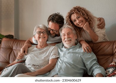 Happy multigenerational family group sitting on sofa at home while spending time together. Four handsome bonding people, two generations looking at the camera - Powered by Shutterstock