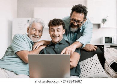 Happy multigenerational family sitting on sofa using laptop together - grandfather with mature son and young grandson enjoying carefree moments together - Powered by Shutterstock