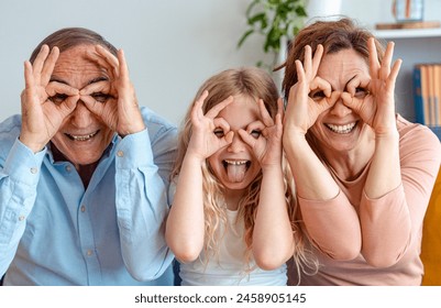 Happy multi-generational family smiling at camera together - Grandfather, grandchild and mother having fun in the living room - Childhood and human relationship concept - Powered by Shutterstock