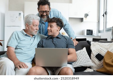 Happy multigenerational family of three males sit together on the couch smiling and looking at laptop together. Grandfather, mature son and young grandson share positive moments in total relaxation - Powered by Shutterstock