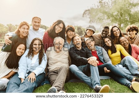 Happy multigenerational people having fun sitting on grass in a public park - People diversity concept