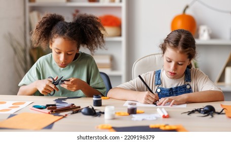 Happy Multinational Children Girls Making Halloween Home Decorations Together, Kids Painting Pumpkins And Making Paper Cuttings