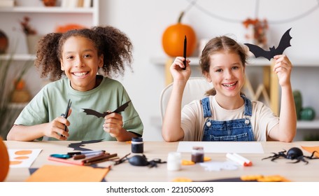 Happy Multinational Children Girls Making Halloween Home Decorations Together, Kids Painting Pumpkins And Making Paper Cuttings