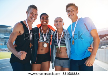 Happy multiracial athletes celebrating victory while standing together on racetrack. Group of runner with medals winning a competition.