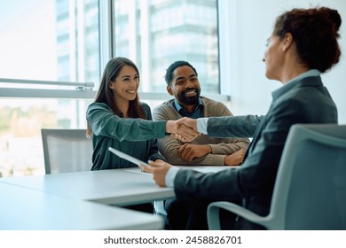 Happy multiracial couple came to agreement with insurance agent during a meeting in the office. Women are shaking hands. Copy space. - Powered by Shutterstock