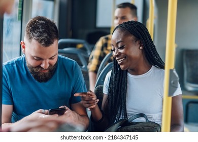 Happy multiracial couple of friends sitting in a bus and using a smartphone while chatting during their ride. Public transportation. Browsing social network. Focus on beautiful african american woman - Powered by Shutterstock