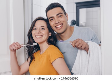 happy multiracial couple holding toothbrushes in bathroom - Powered by Shutterstock