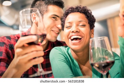 Happy multiracial couple of lover drinking red wine at fashion restaurant - Handsome man whispers soft kisses in beautiful woman ear - Relationship concept with boyfriend and girlfriend on warm filter - Powered by Shutterstock