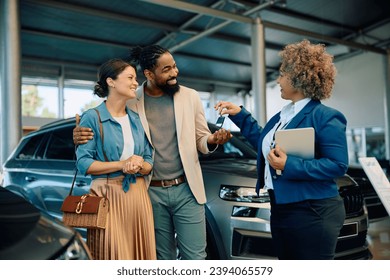 Happy multiracial couple receiving keys of their new car from saleswoman in showroom.  - Powered by Shutterstock