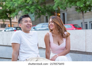 Happy Multiracial Couple Sitting Relaxed On A Urban Park