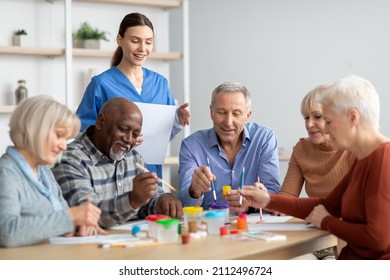 Happy multiracial elderly men and women sitting around table and drawing at nursing home, doing arts and crafts together, young lady nurse assisting group of senior people, copy space - Powered by Shutterstock