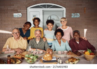 Happy Multiracial Extended Family Gathering For Lunch At Dining Table On Patio And Looking At Camera. 