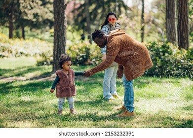 Happy Multiracial Family Having Fun While Spending Free Time Together In The Park. Multicultural Joy And Love Concept With Different Race. Parents Together With Their Daughter In The Park.