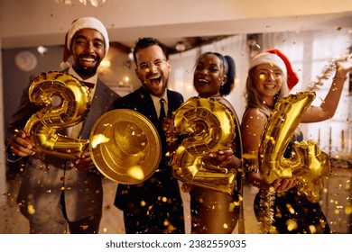 Happy multiracial friends with 2024 golden balloons having fun on New Year's party at home looking at camera.