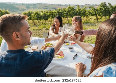 Happy multiracial friends cheering at summer dinner with vineyard in background - Adult people enjoying white wine glass at countryside resort - Focus on closeup hands - Powered by Shutterstock