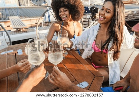 Happy multiracial friends cheering with wine at boat party outdoor - Focus on right girl hand