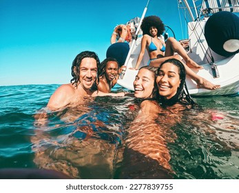 Happy multiracial friends doing selfie swimming in the sea with sail boat in background - Soft focus on center girl face - Summer and travel concept - Powered by Shutterstock