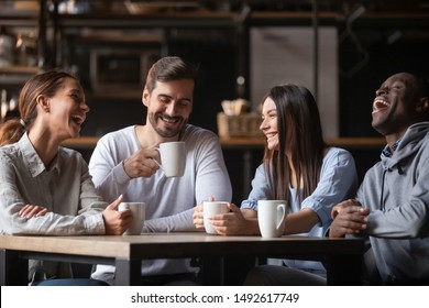 Happy multiracial friends group laugh drink tea in cafe, diverse young students talk enjoy coffee at coffeehouse meeting, multicultural people sit at table having fun together multi-ethnic friendship