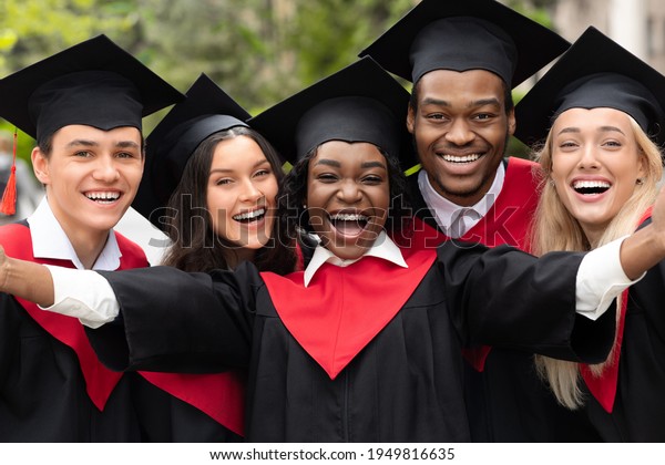 Happy\
multiracial group of students in graduation dresses and hats taking\
selfie together, posing at university campus, enjoying and\
celebrating graduation, closeup\
portrait