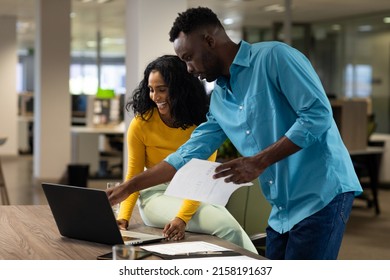 Happy multiracial male and female business colleagues discussing over laptop at modern workplace. unaltered, business, technology, teamwork and modern office concept. - Powered by Shutterstock